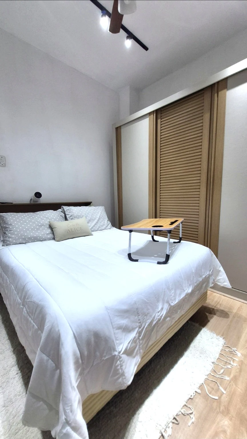 Cama de casal com roupa de cama branca, apoio para notebook e armário de madeira
