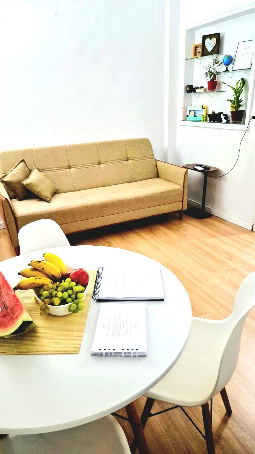 Sofá da sala, prateleiras decoradas e mesa redonda de refeições